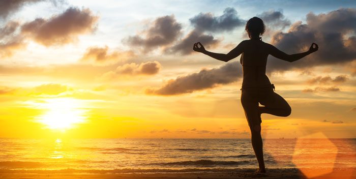 Woman standing in a yoga position on the beach as the sun rises. 