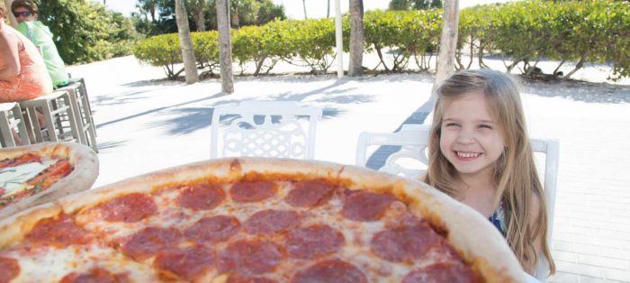 Girl looking at a large pizza on the beach.