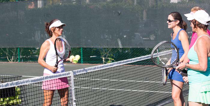 Ladies around the net on a clay tennis court.