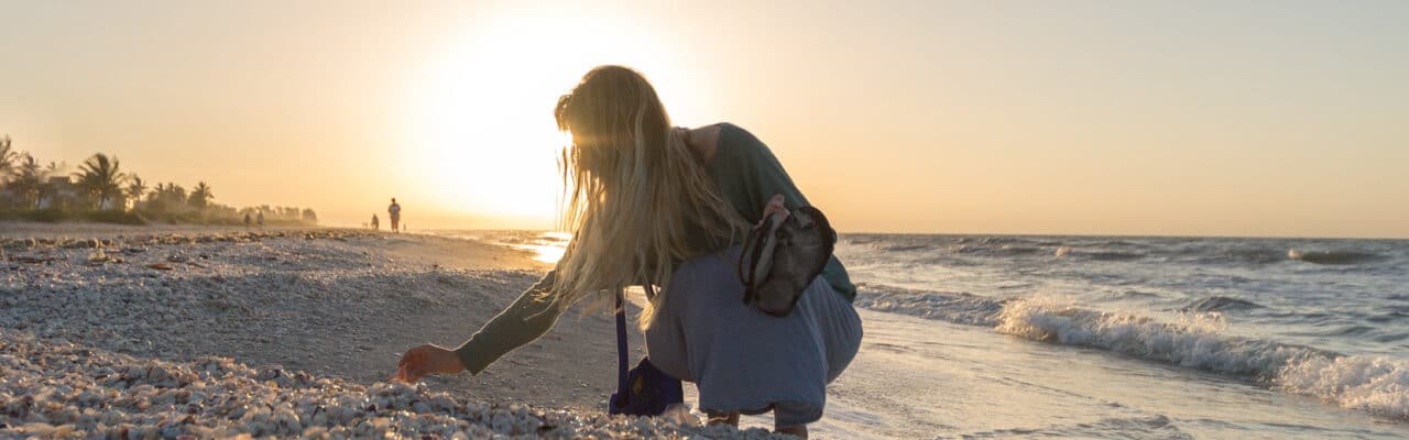 woman crouching down to shell pile at tide line on sanibel island at sundial resort