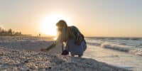 woman crouching down to shell pile at tide line on sanibel island at sundial resort