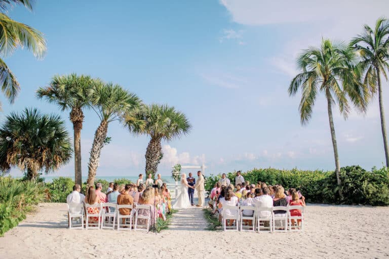 beach wedding ceremony set up with white chairs and altar, palm trees and gulf in background