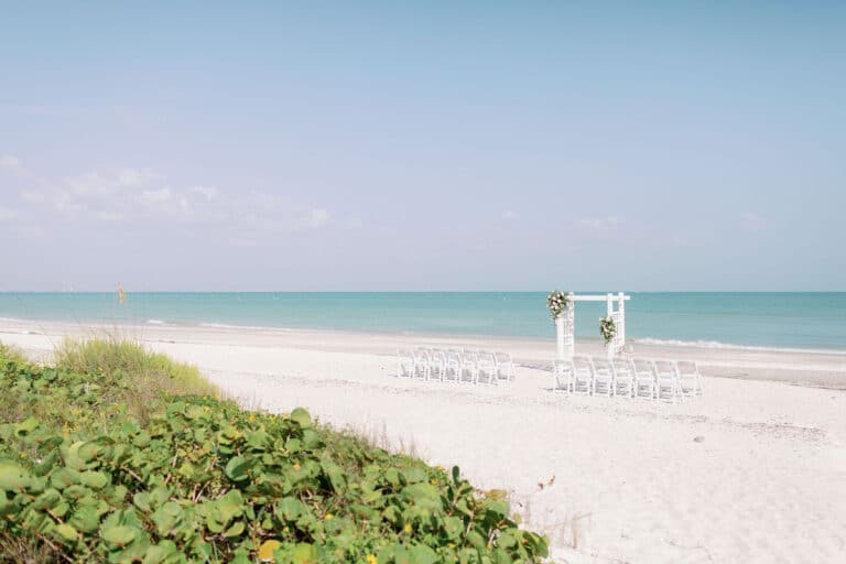 beach wedding ceremony set up with white chairs and altar, gulf in background