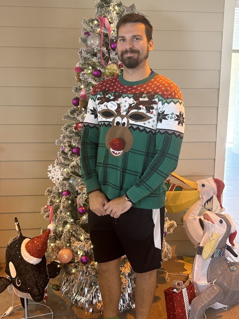 sundial staff member josh posing in reindeer christmas sweater in front of tree and decor