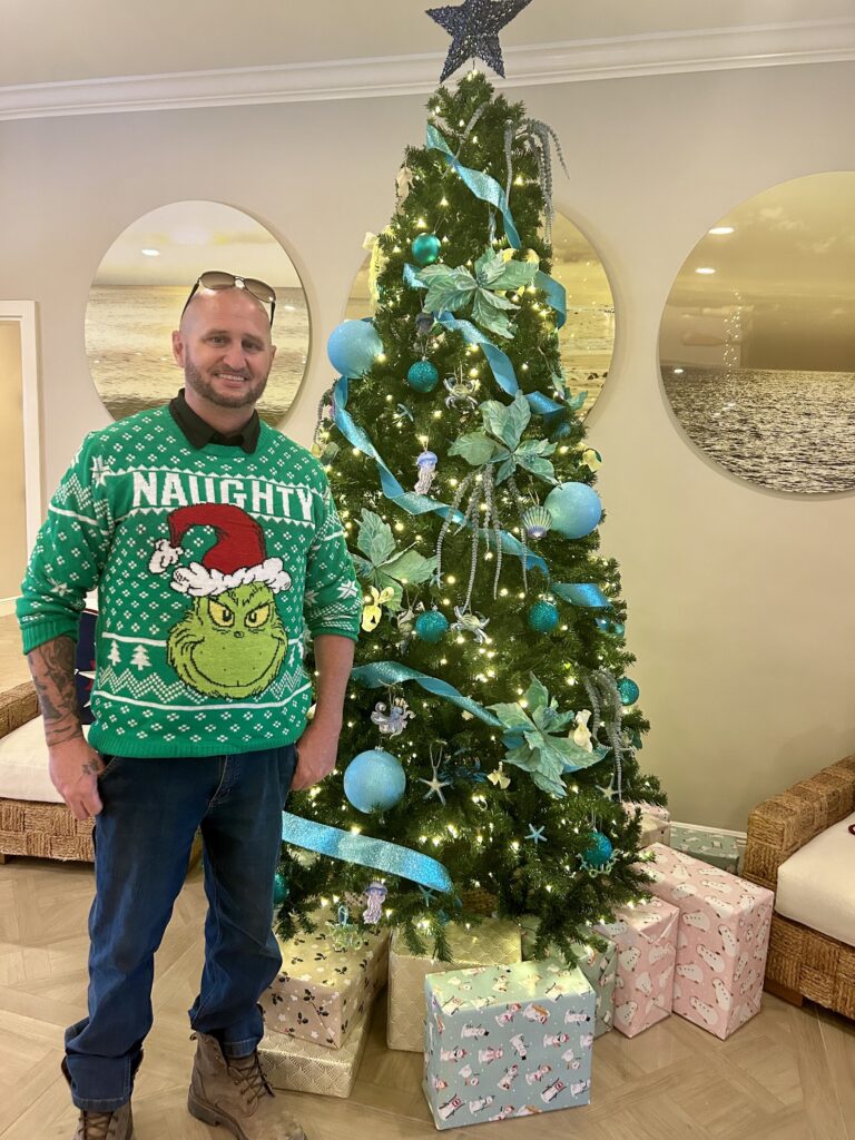 sundial staff member in grinch sweater posing with lobby christmas tree