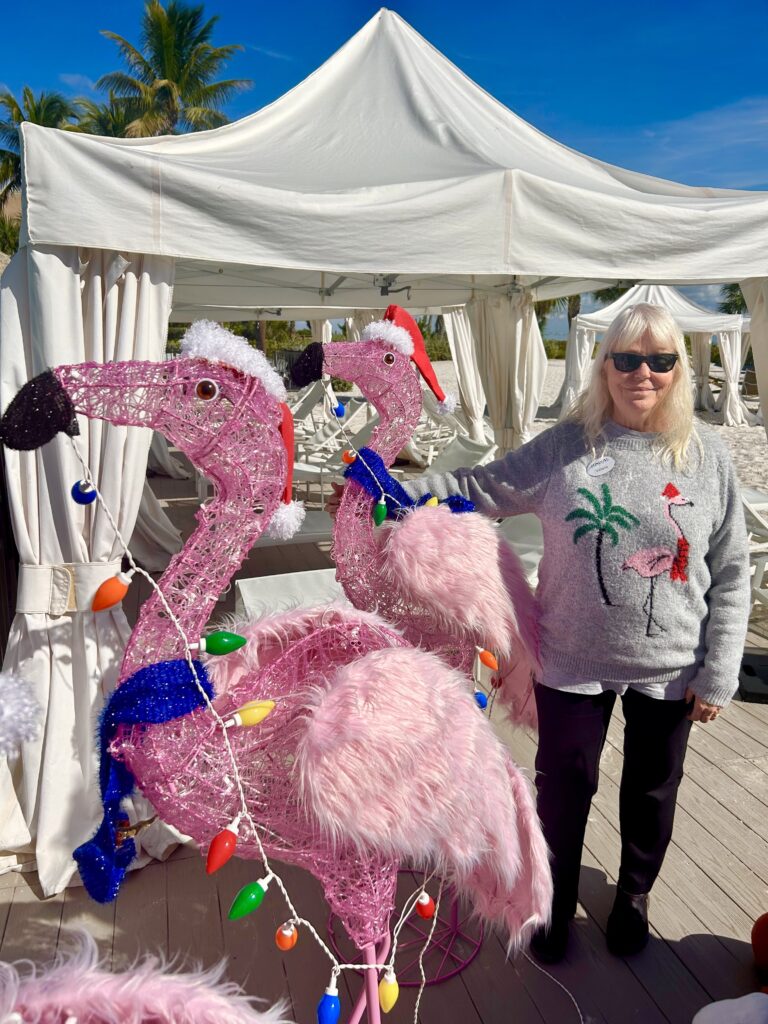 sundial staff member in flamingo christmas sweaters poswing with christmas flamingo statues on the pool deck by the cabanas