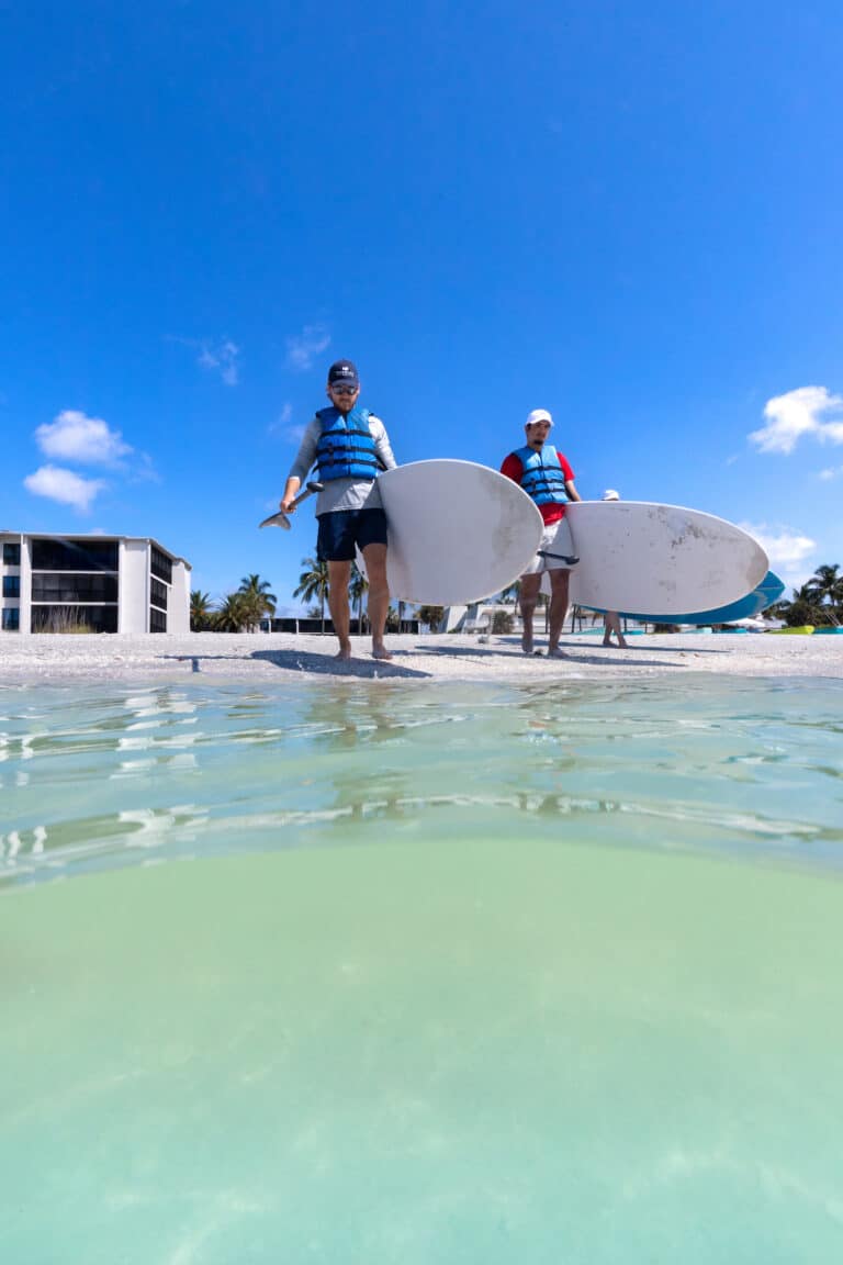 two man carrying paddleboards into the water