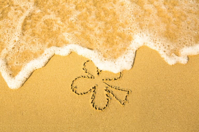 four leaf clover shamrock drawn in sand with water washing over