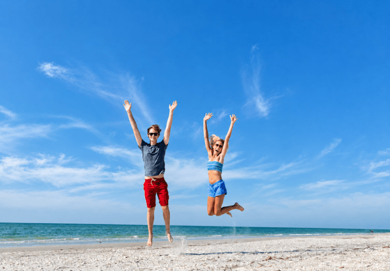 two young people jumping for joy on the beach in front of sundial resort sanibel island v2