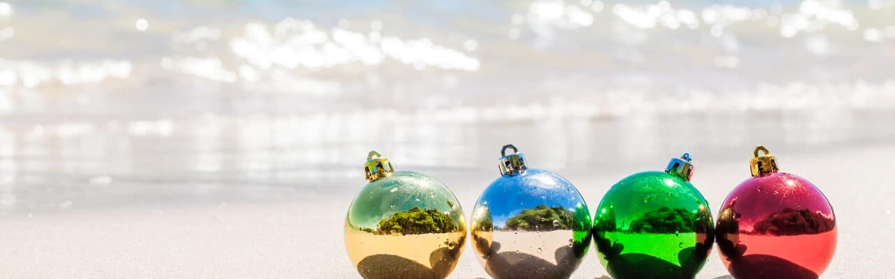 colorful christmas ornaments on the sand with cater in the background crop